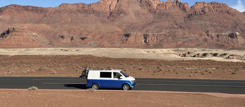 Weiß blauer VW Bus Camper mit Fahrradträge auf einer Straße in der Wüste