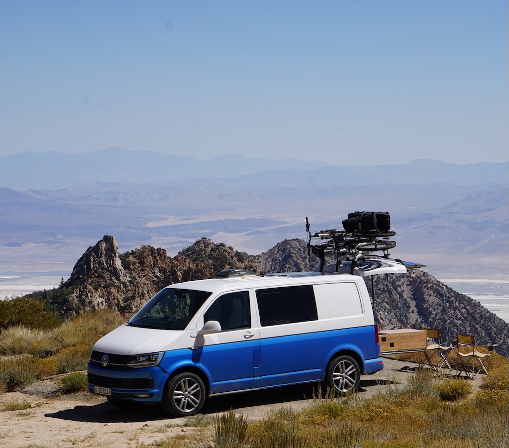 Weiß blauer VW Bus Clever Camper mit Heckküche und Fahrrädern in weitläufiger Natur