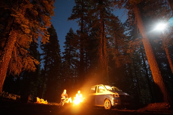 Personen neben Camper am Lagerfeuer im Wald in der Nacht
